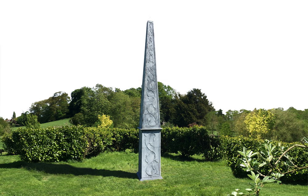 Tall zinc-coated steel obelisk sculpture standing on a lawn in a landscaped garden
