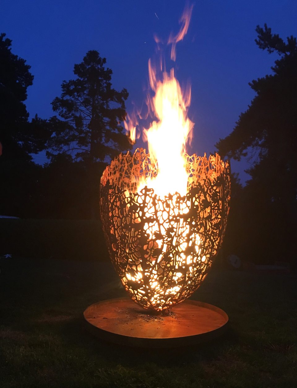 Large Filigree Fire Basket with a tall fire burning at night, making beautiful silhouettes against the steel latticework.
