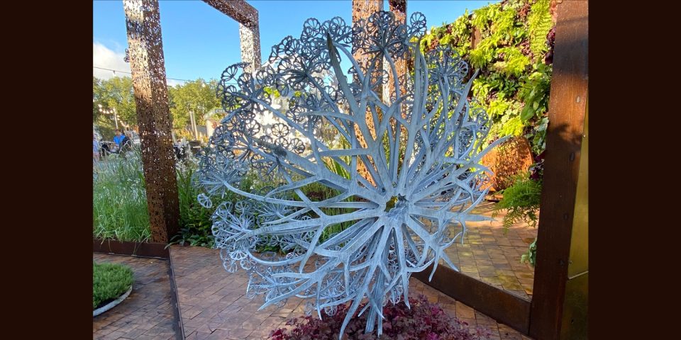 Aura sculpture from the back showing the dynamic 360 structure, with metal parts like swords crossed in a geometric pattern.