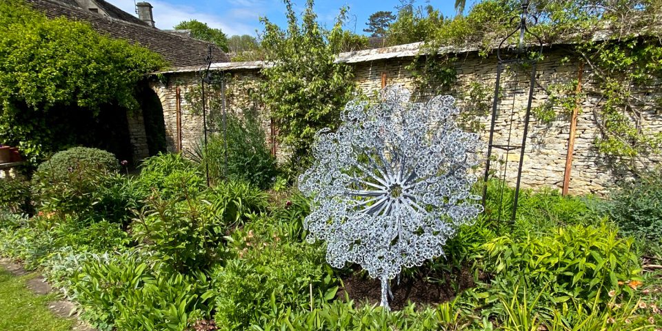Aura sculpture set in the planted border of a formal garden echoing the plant forms in the metal shapes.