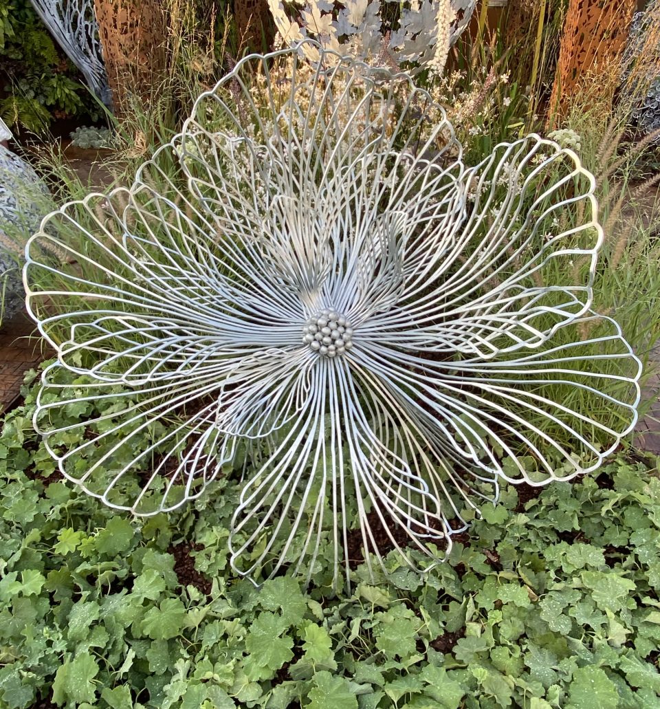 A small Flora sculpture on a bed of Alchemilla with Gaura and taller grasses visible behind.