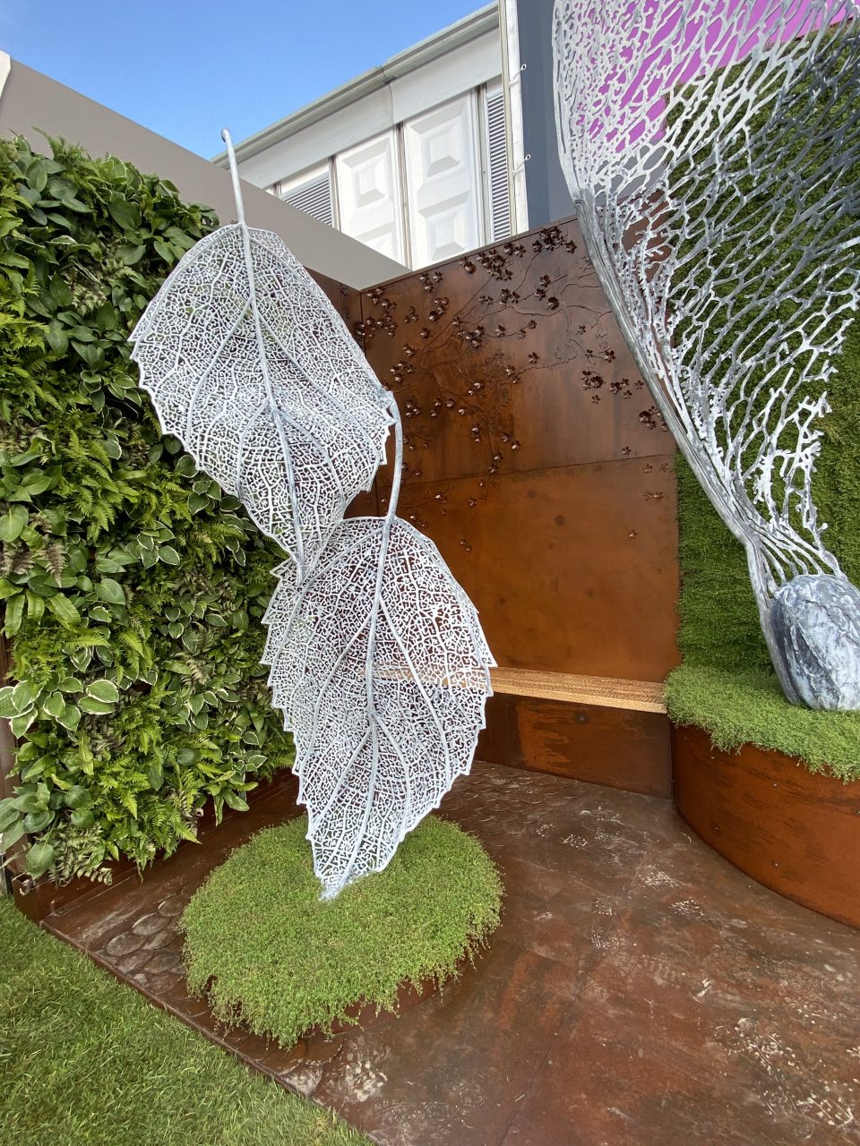 A Falling Leaves sculpture on our tradestand at the Chelsea Flower Show. standing out against a rust wall and a living wall.