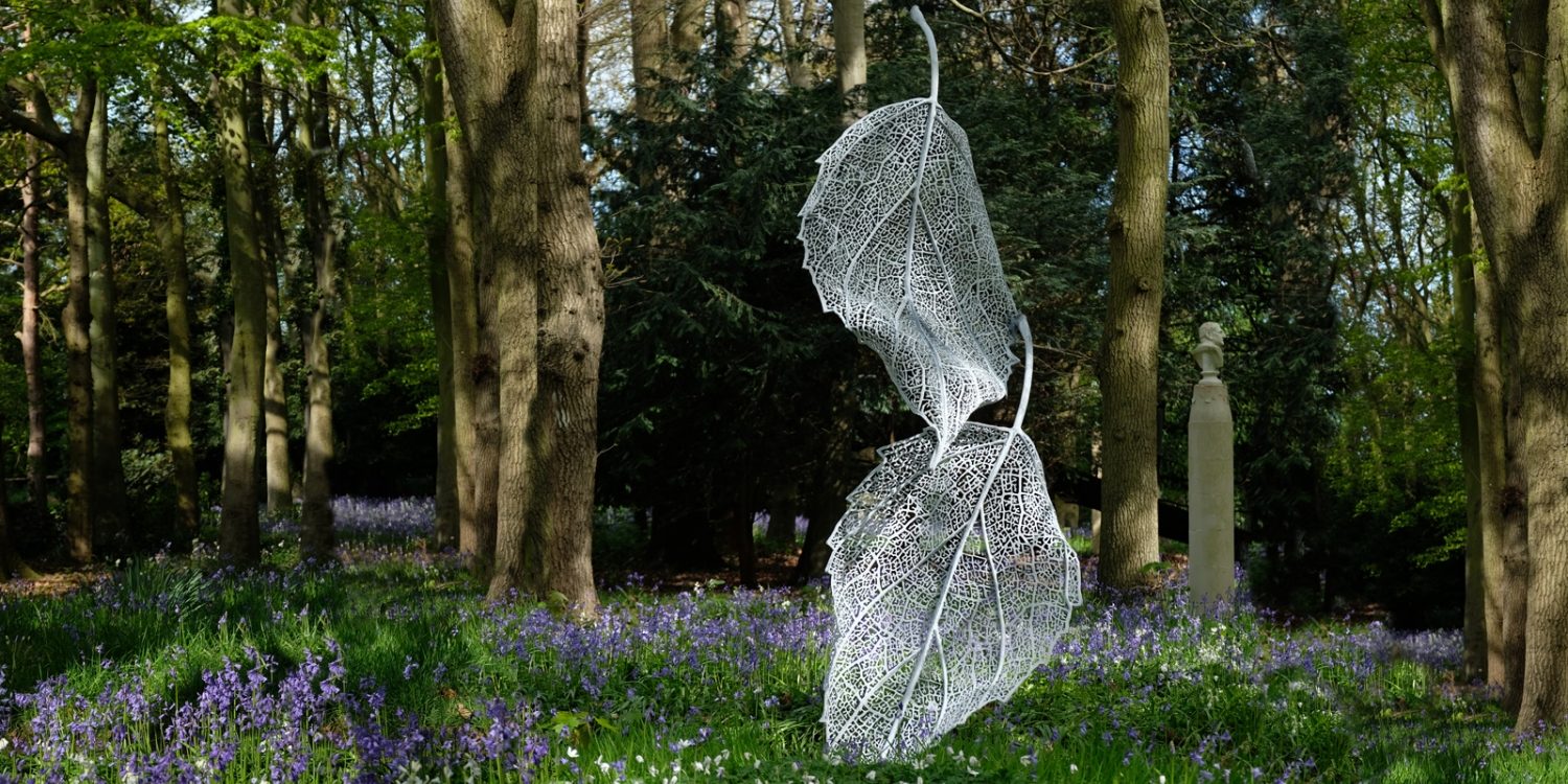 A Falling Leaves sculpture in an open woodland with its lacy, filigree structure standing out against the dark background.
