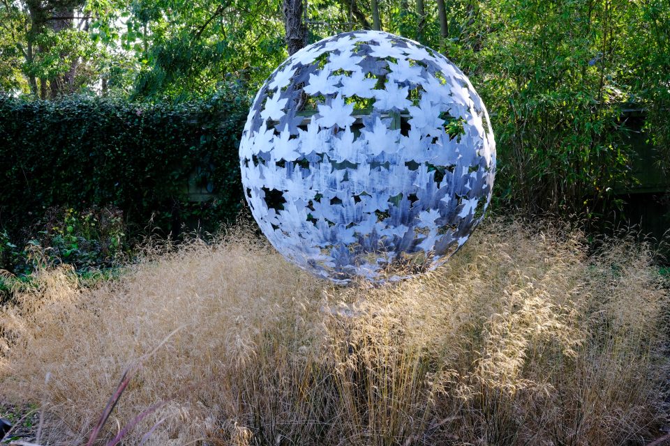A 120cm diameter leaf sphere sculpture set in a meadow of grasses which hide the plinth and make it look like it is floating.