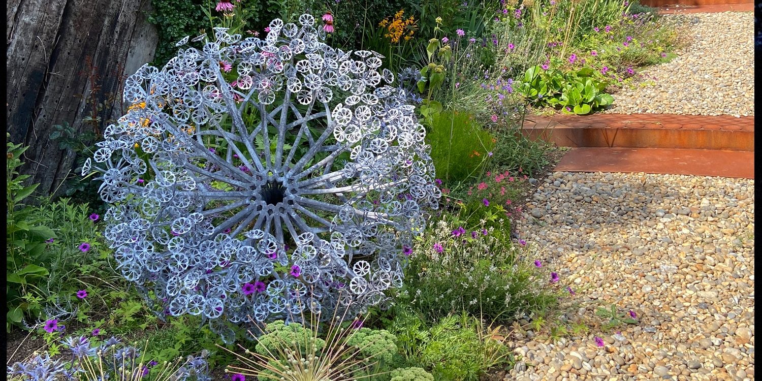 Aura sculpture set in a summer planted border next to a gravel path, adding height and structure to the border.