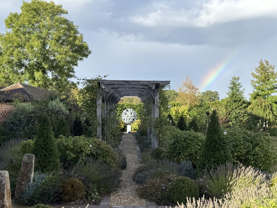 Leaf Sphere sculpture placed as a focal point at the end of a wooden pergola on a gravel path surrounded by perennial shrubs